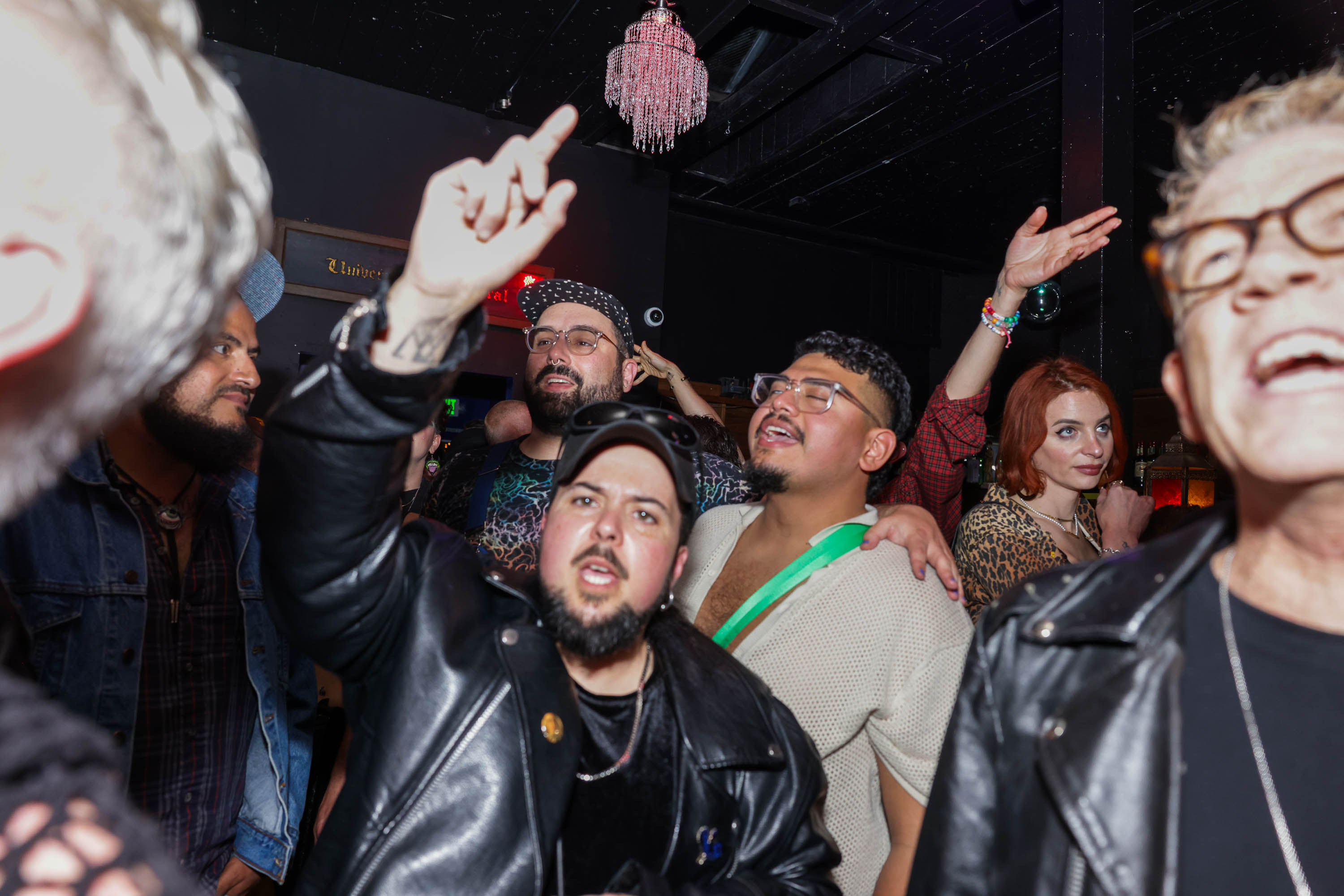 a crowd of people on a dancefloor sing enthusiastically with their hands aloft