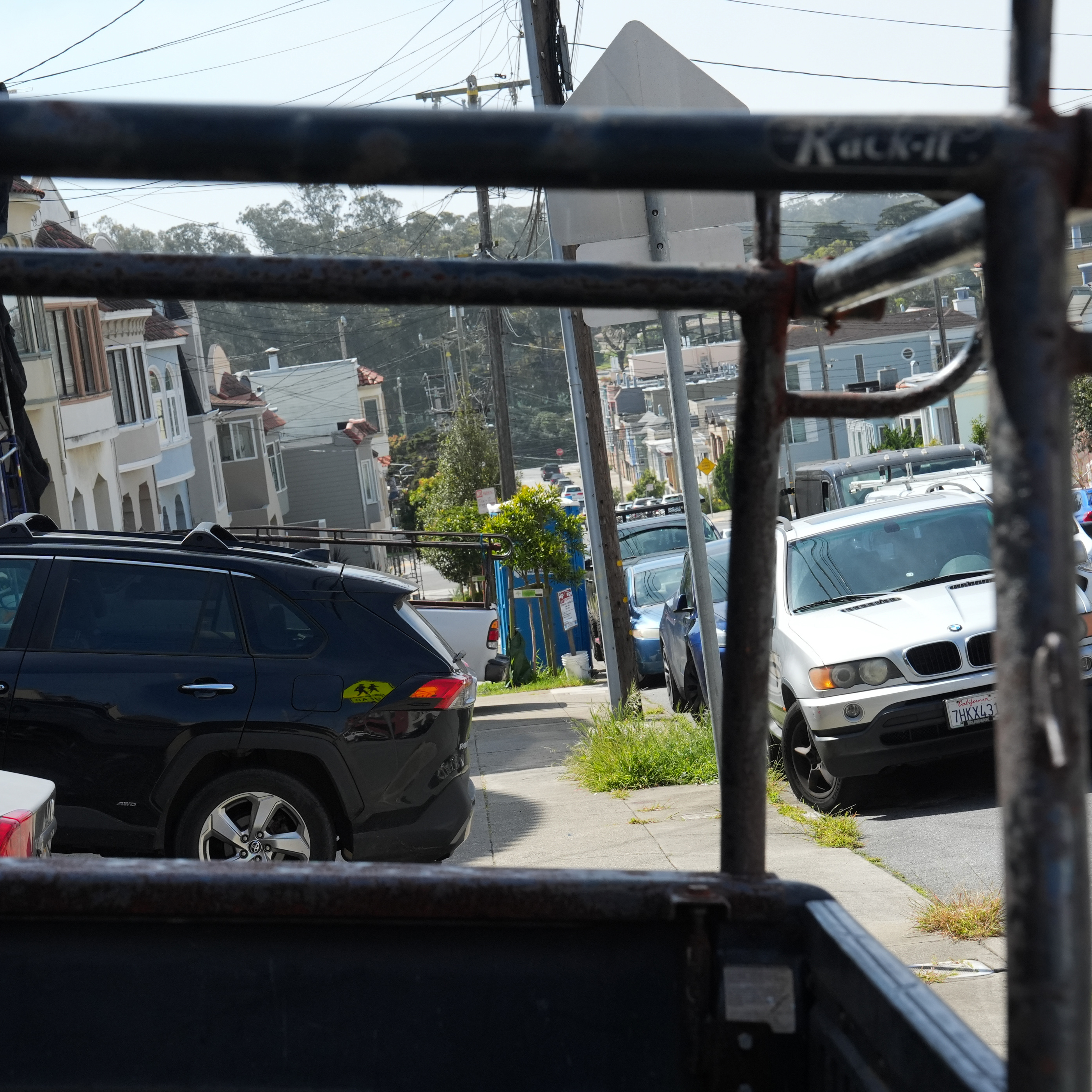 View from a cable car showing a sunny street lined with cars and houses.