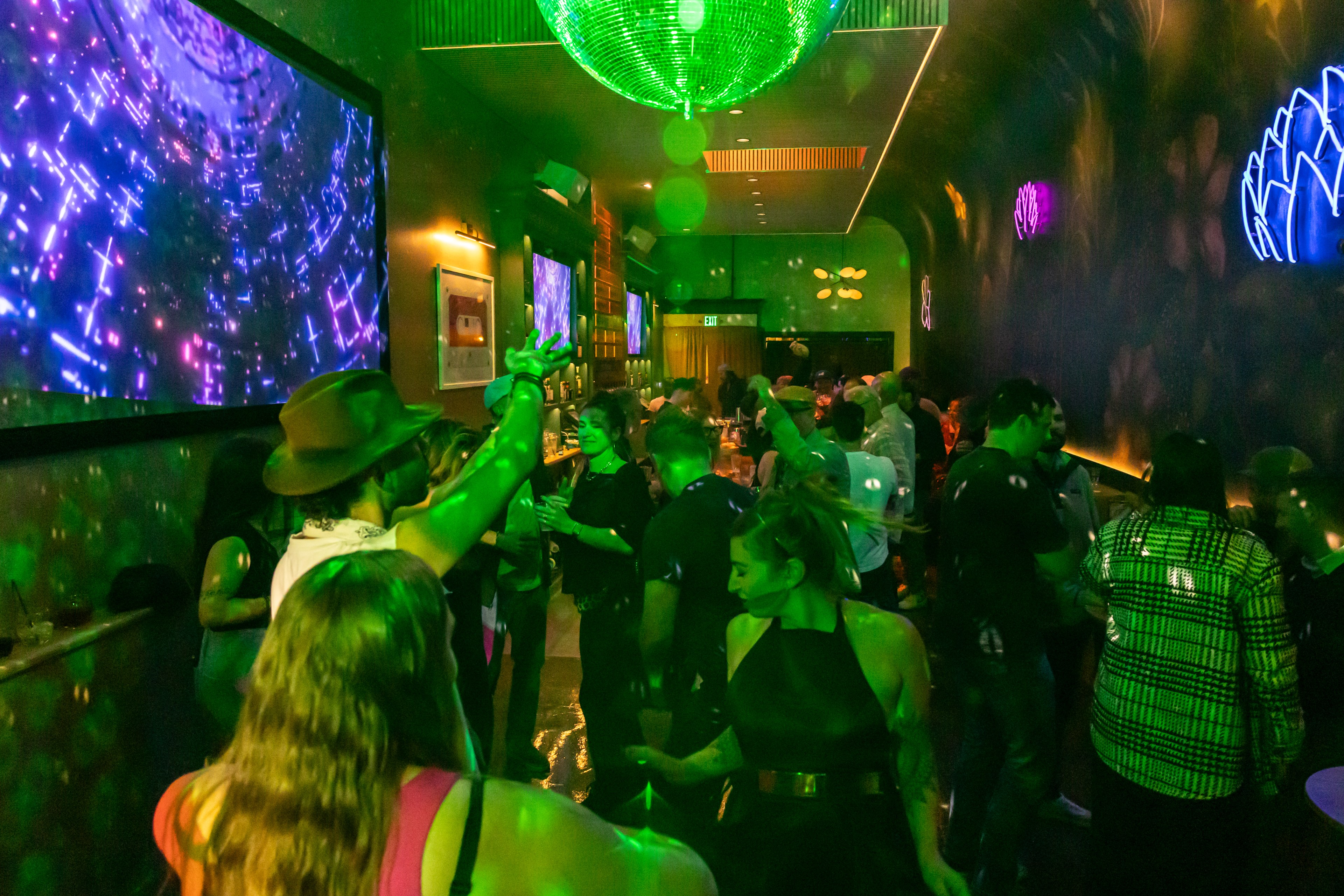 People dance in a dark room under hanging disco balls.