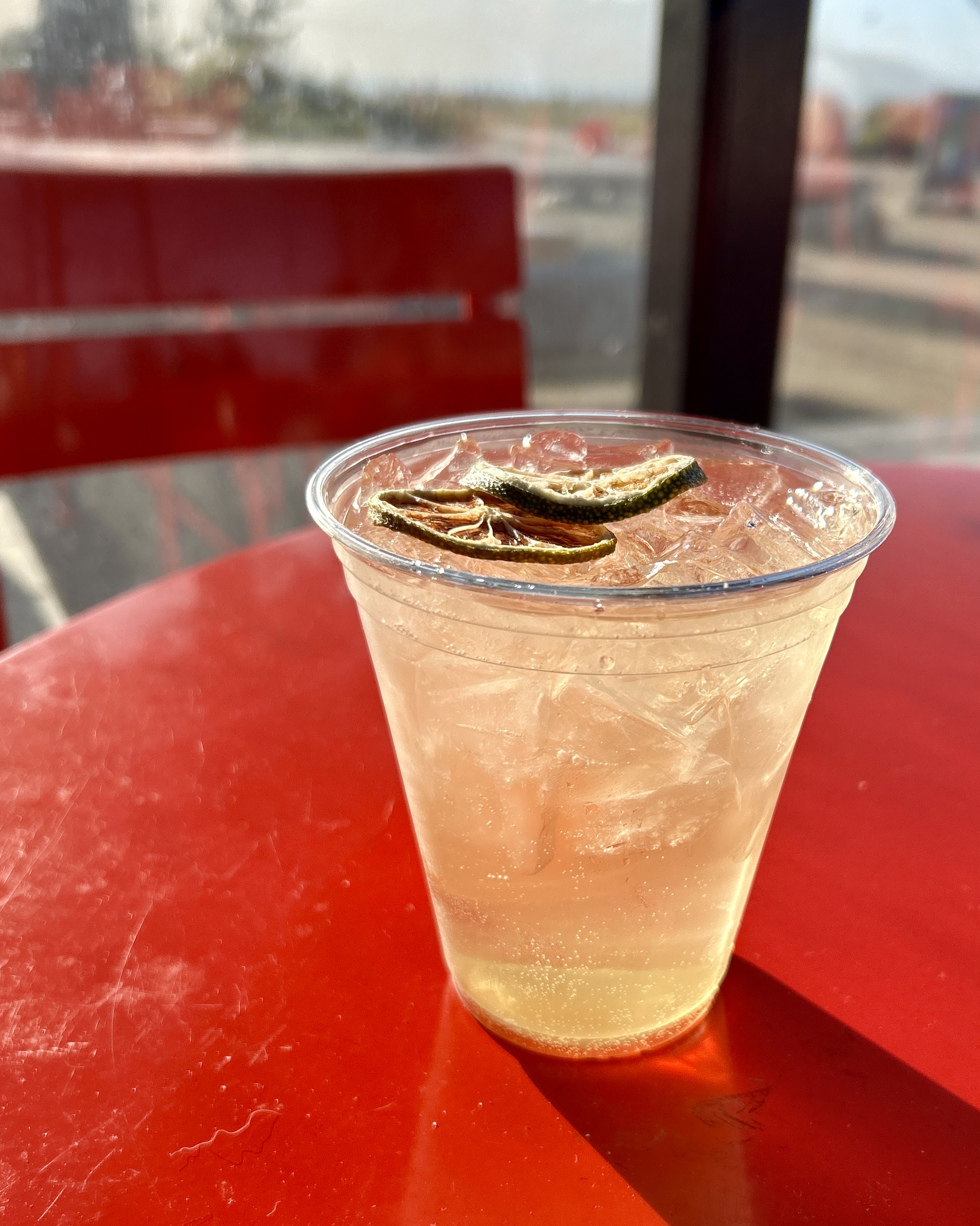 A cocktail in a plastic cup sits on a red table.