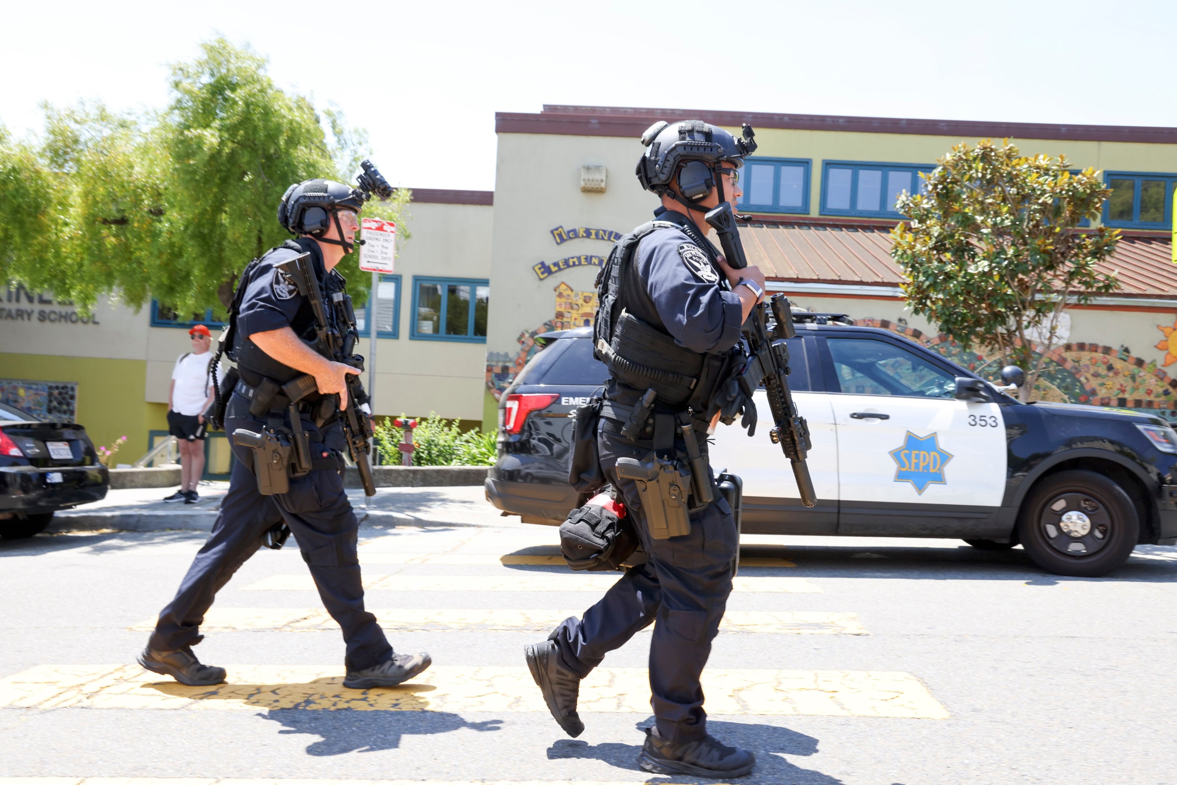 Police officers wearing helmets and carrying rifles hurry down a street.