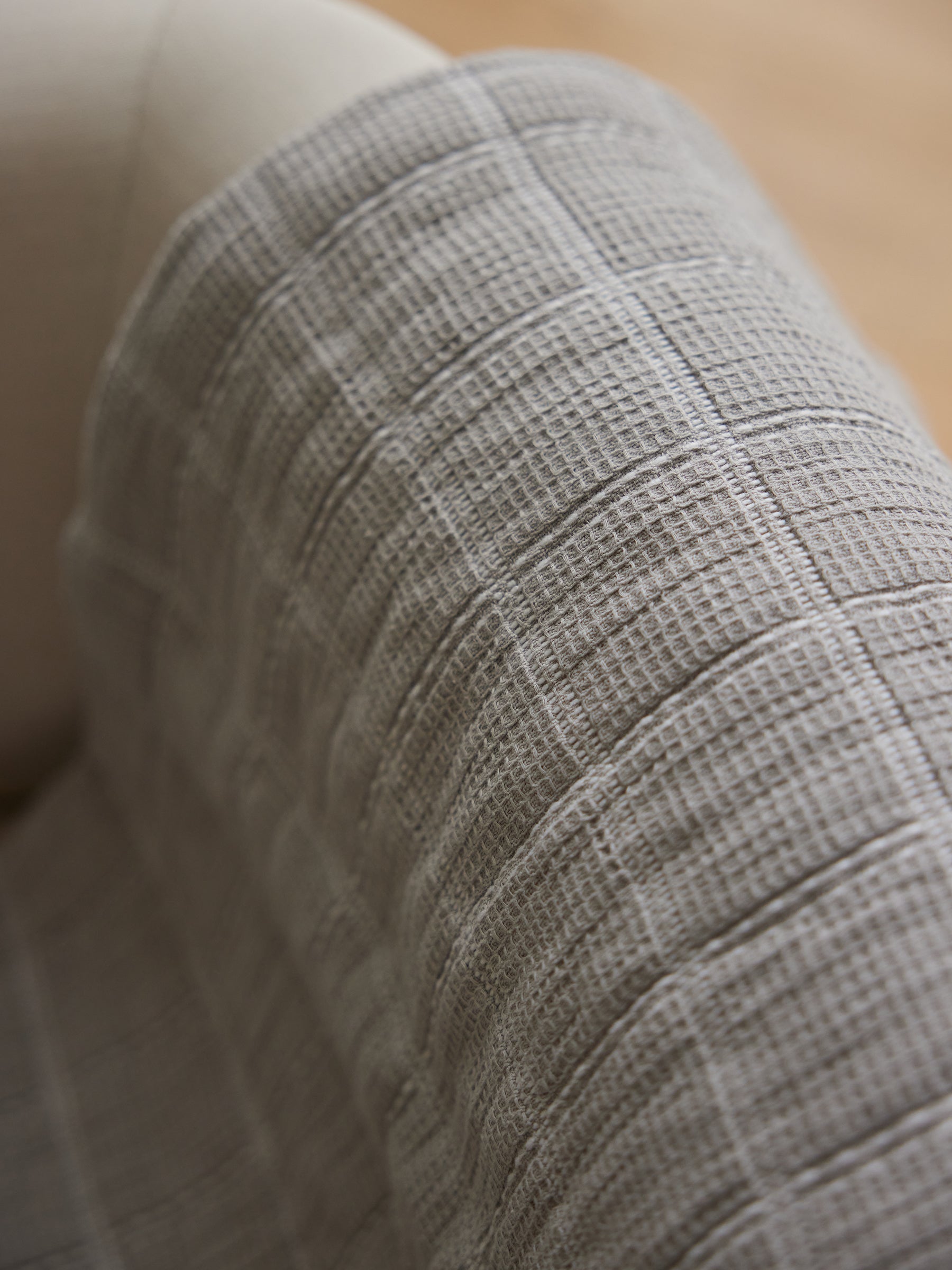 A close-up image of Cozy Earth's beige-colored Waffle Windowpane Blanket draped over part of a light-colored upholstered chair. The blanket's grid-like, waffle pattern creates a soft and cozy appearance. The background is softly blurred. |Color:Dove Grey