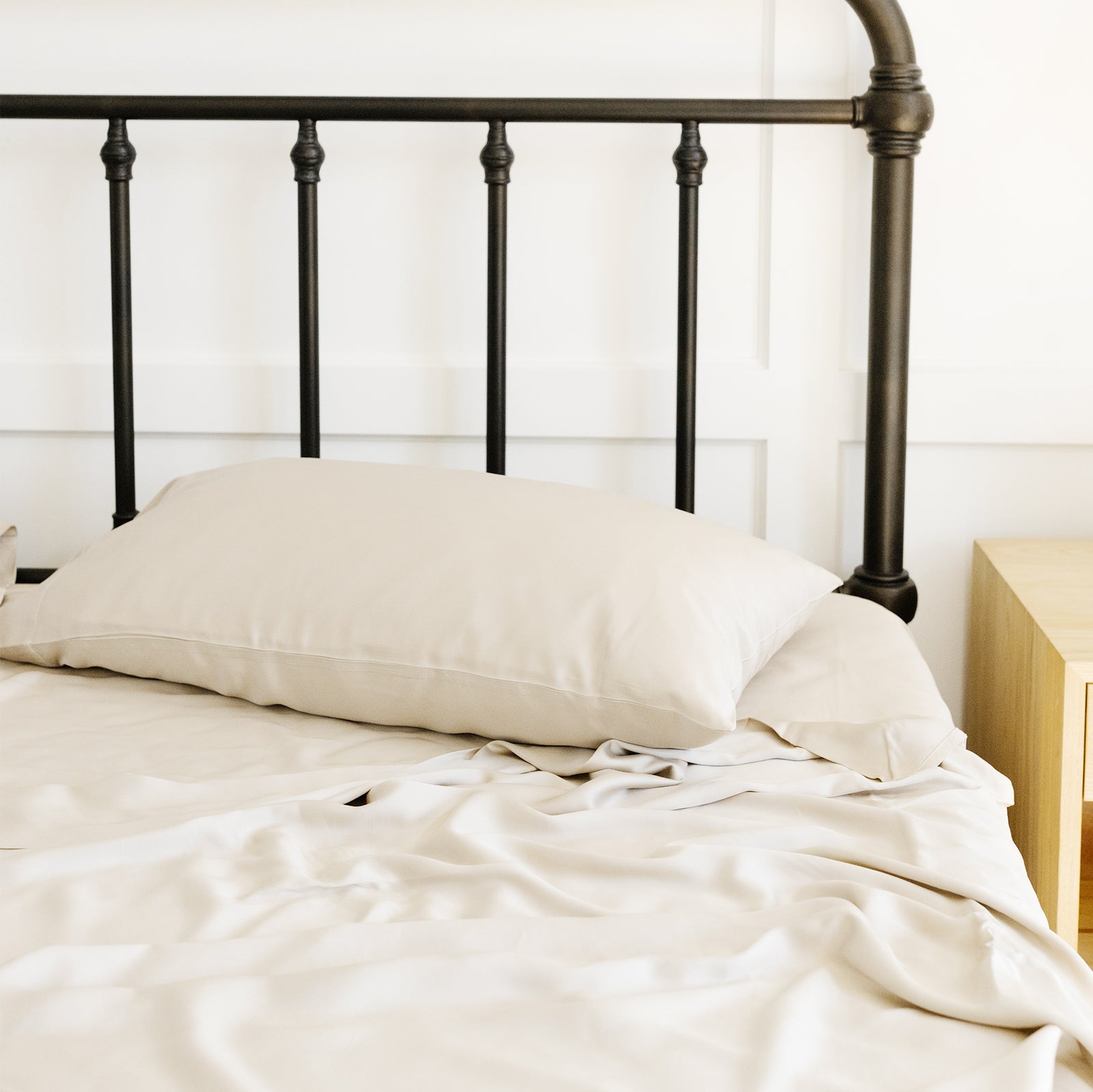 Unmade bed with oat bedding and black frame 