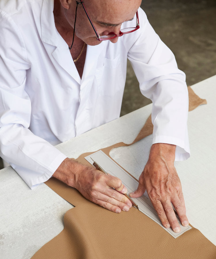 Person in lab coat measuring and cutting leather with a ruler and knife