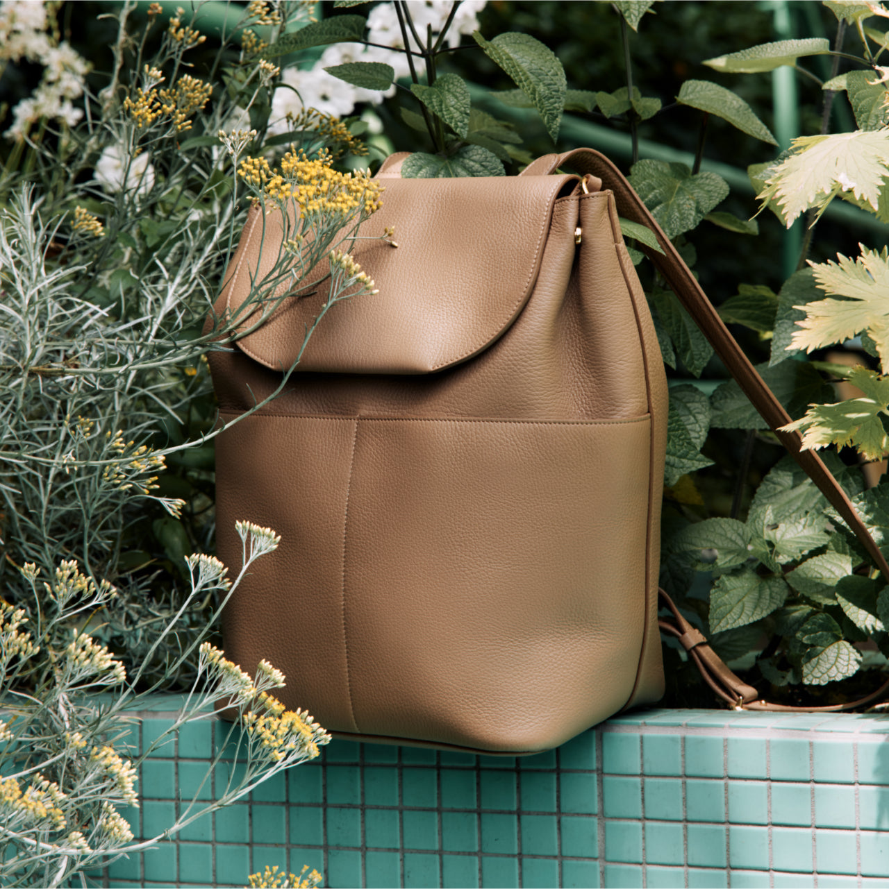 Backpack on a tiled surface surrounded by plants.