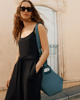 Person in sunglasses carrying a large handbag and standing in front of a building.