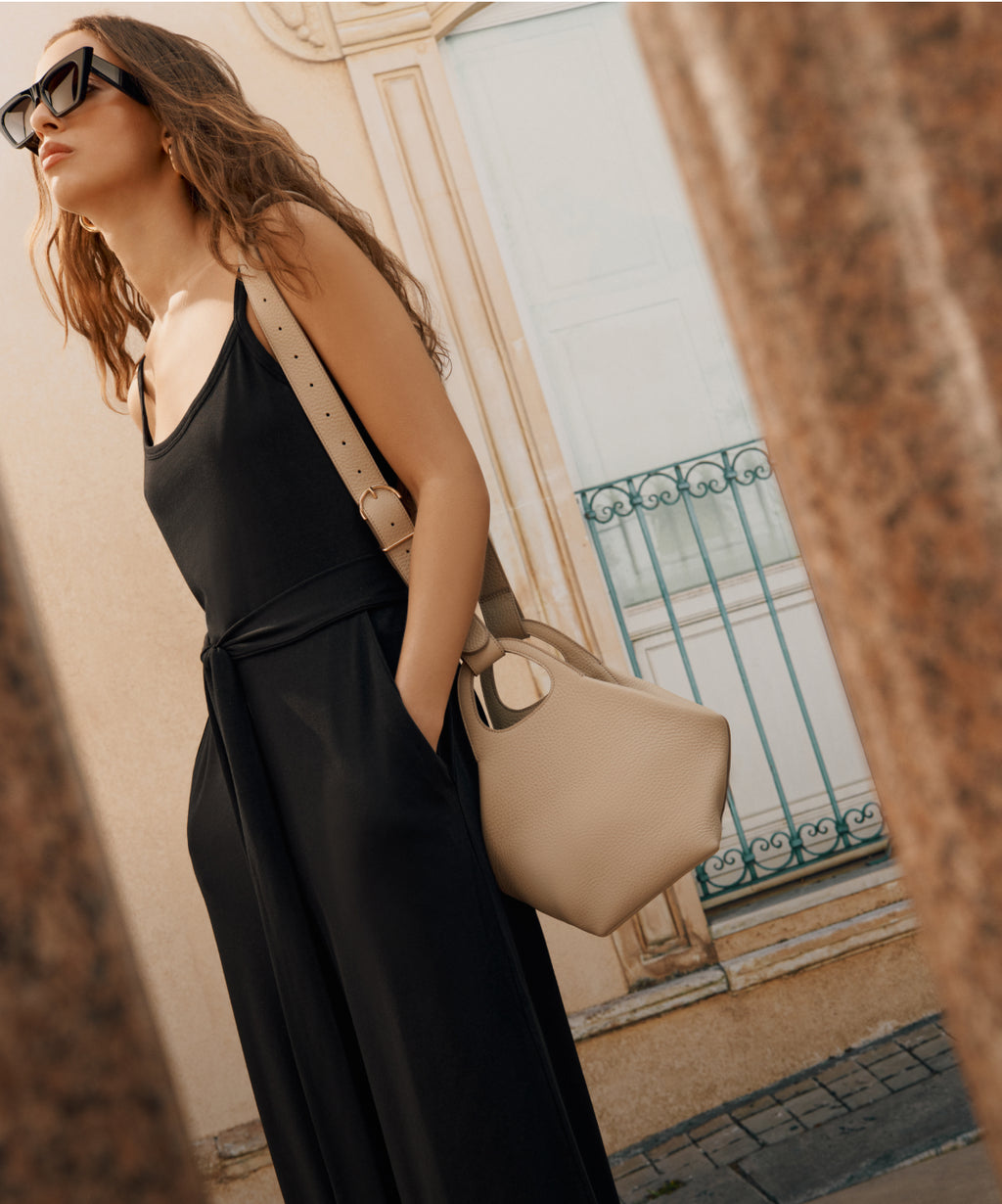 Person posing with a shoulder bag, wearing sunglasses and a sleeveless outfit, standing outdoors.