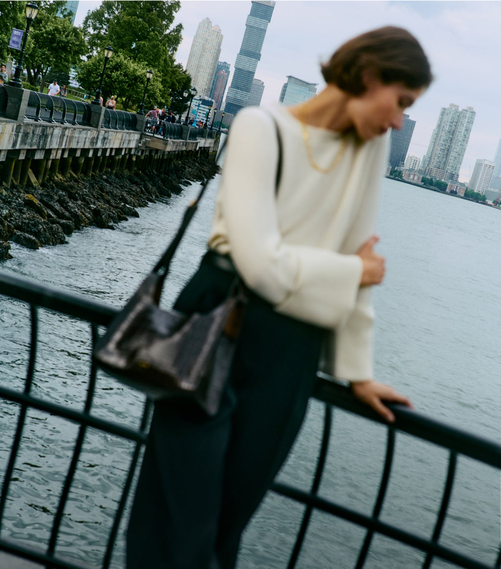 Person leaning on railing by a waterfront with tall buildings in the background