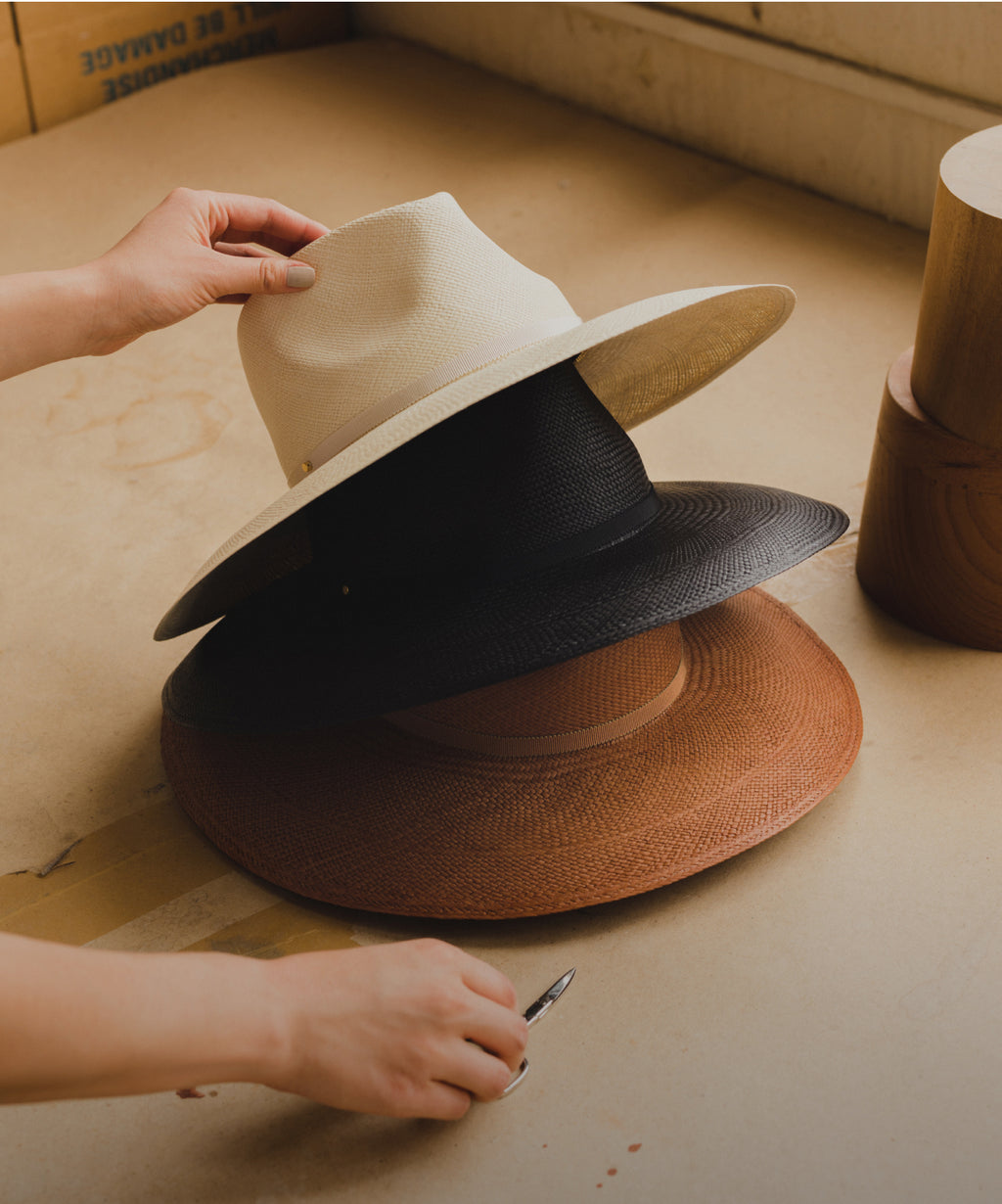 Three wide-brimmed hats stacked on a table with a hand adjusting the top hat.