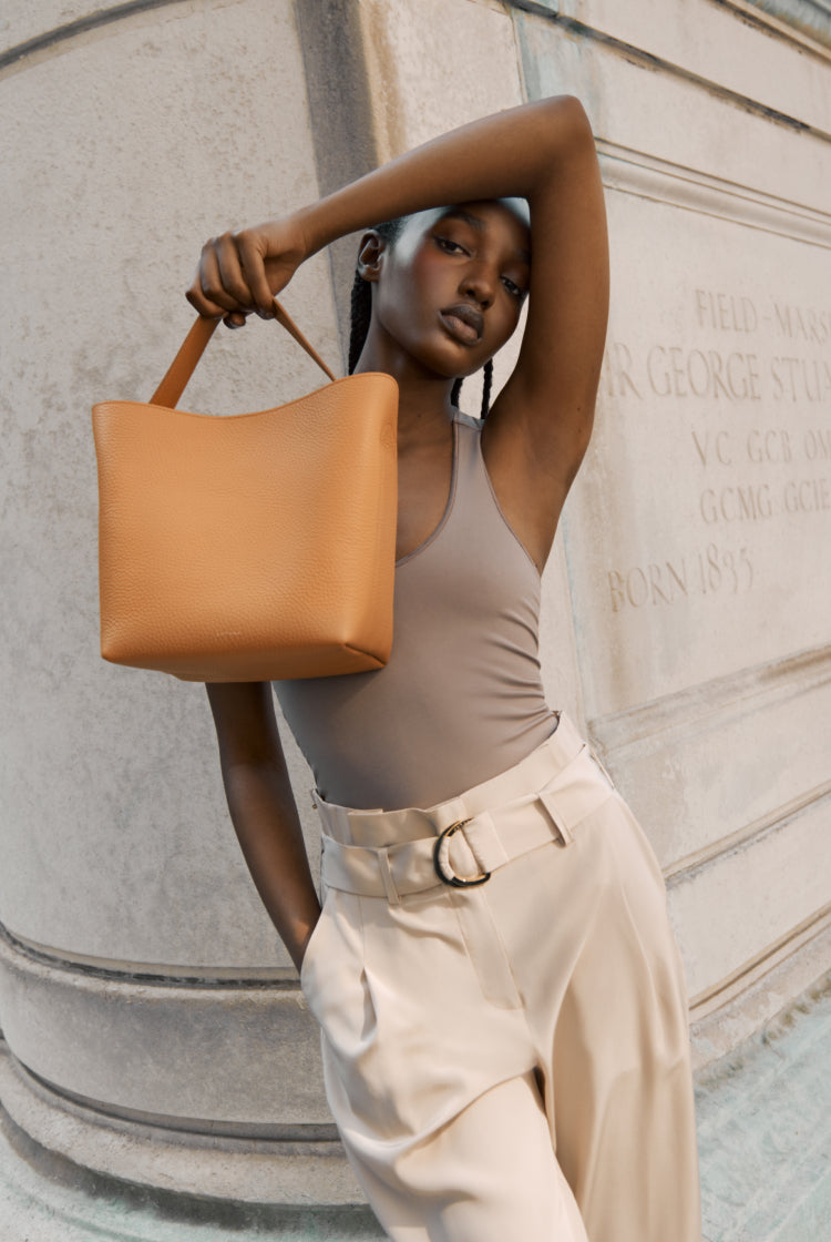 Woman posing with a handbag near a historical wall plaque.