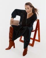 Person sitting on a chair, holding a small clutch, and wearing tall boots.