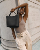 Woman holding a bag, standing by a stone structure with arm raised.