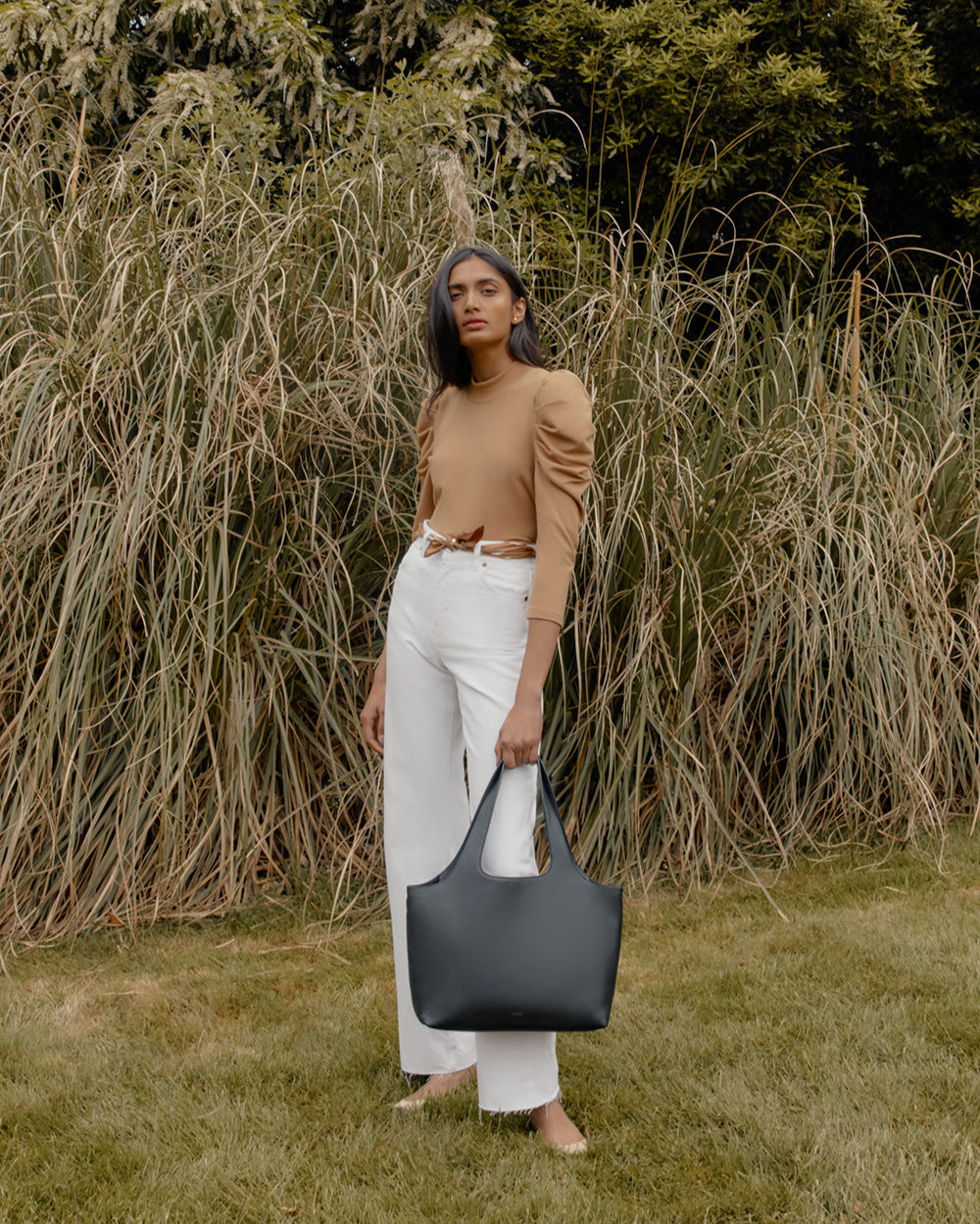 Woman standing in front of tall grass holding a large bag.