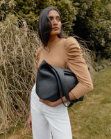 Woman standing outdoors holding a large handbag