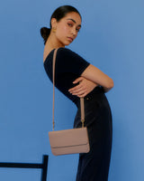 Person posing with a small shoulder bag against a blue background