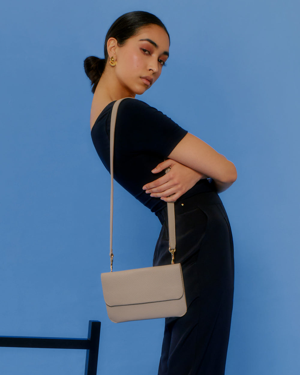Person posing with a shoulder bag against a plain background.