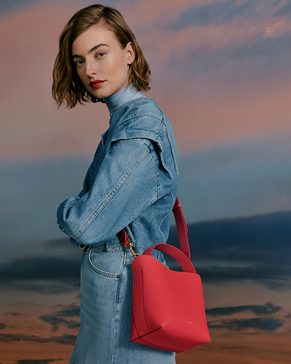 Woman with short hair wearing a jacket and carrying a shoulder bag looking over her shoulder.