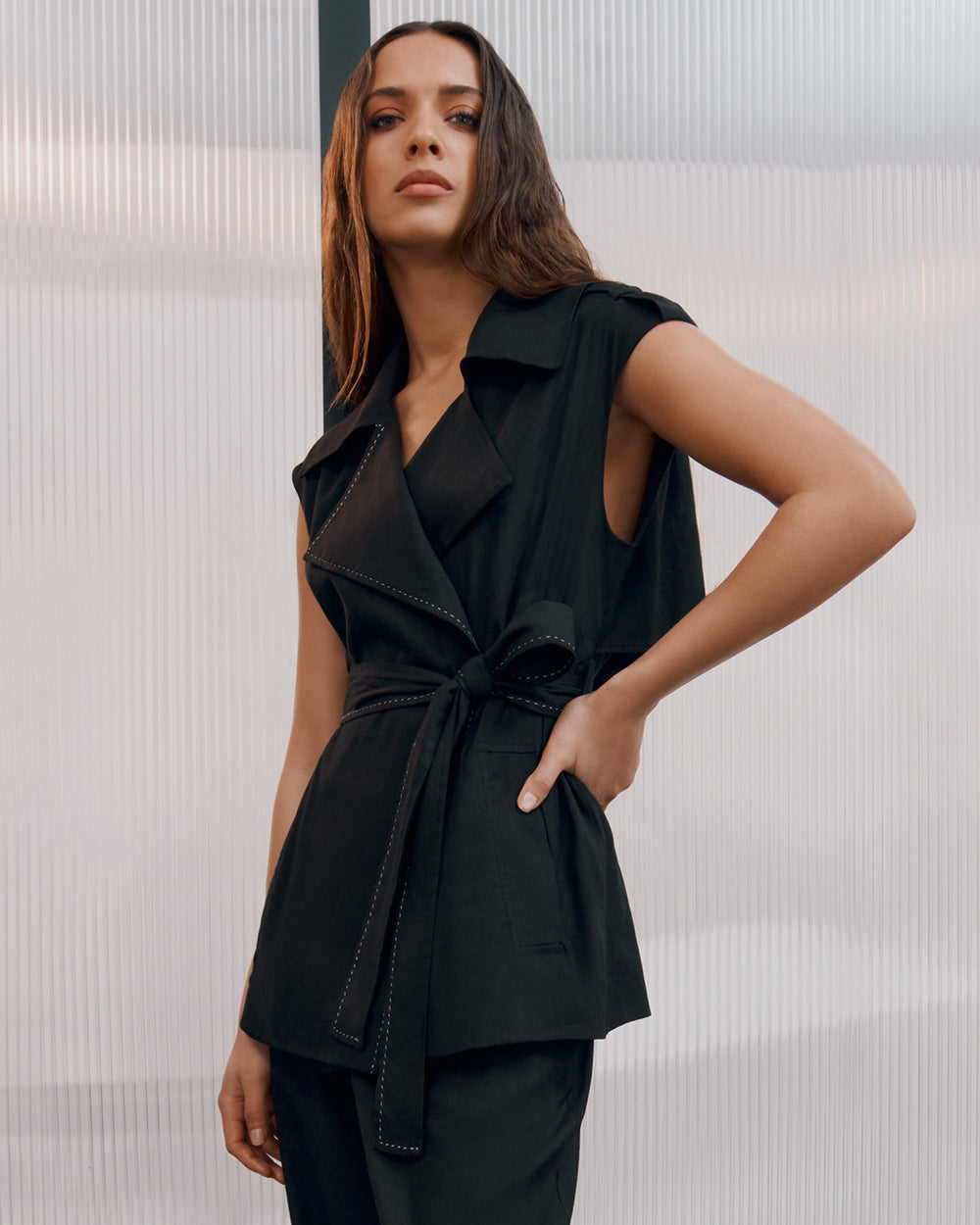 Woman standing with her hand on her hip, wearing a sleeveless top and pants.