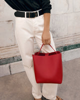 Person holding a tote bag, standing against a wall.