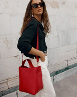 Woman with sunglasses carrying a handbag standing against a wall.