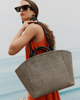 Woman holding a large tote bag, wearing sunglasses and earrings, looking away.