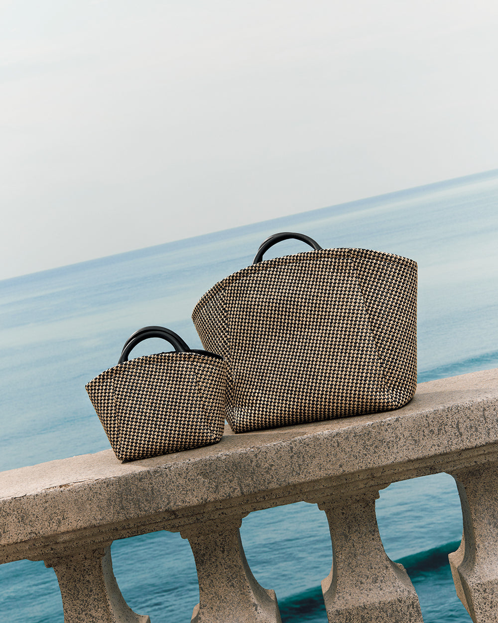 Two handbags on a stone railing overlooking the sea.
