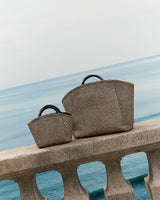 Two handbags on a stone railing overlooking the sea.