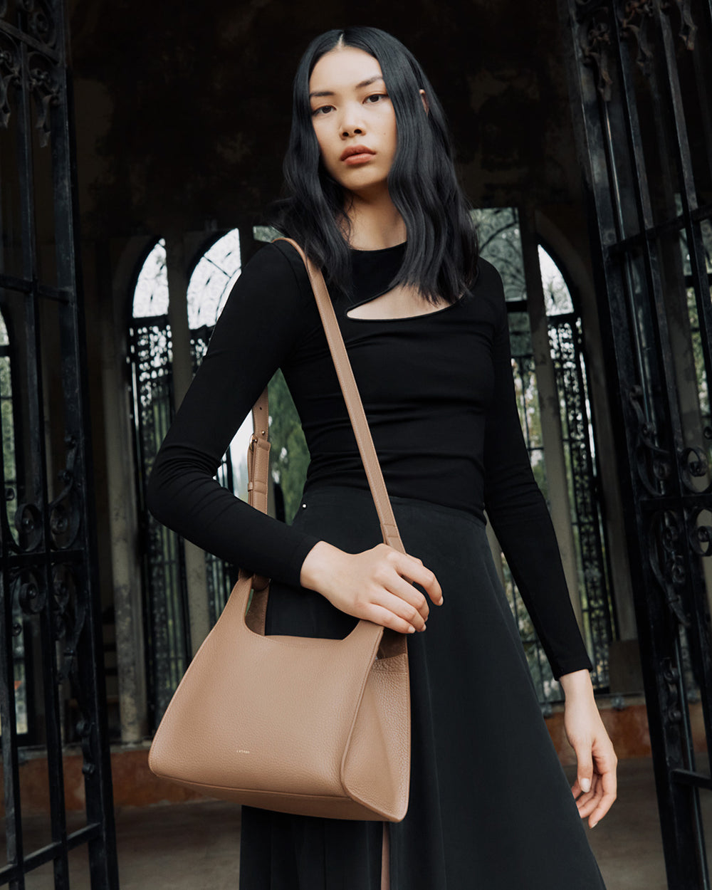 Woman standing by an ornate gate holding a handbag