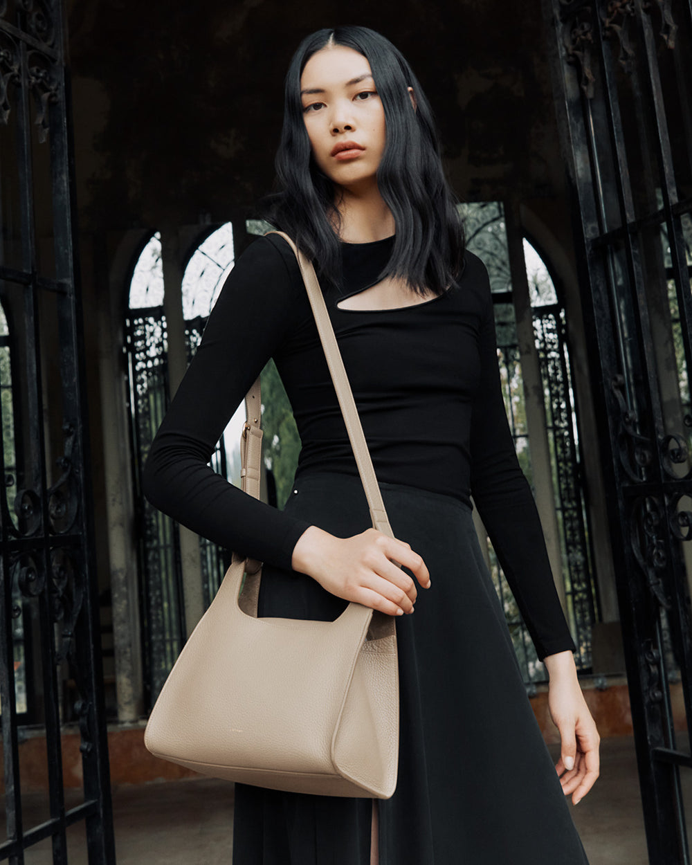 Person standing in front of black iron gates, holding a handbag on their shoulder