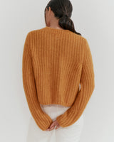 Person standing with back facing the camera, wearing a sweater and pants, hands clasped behind.