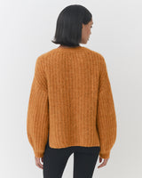 Woman facing away, wearing a sweater and pants, viewed from the back.