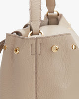 Close-up of a handbag side with a strap attachment and metallic rivets.