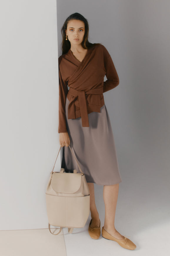 Woman standing with a handbag and wearing a wrap top with a skirt.