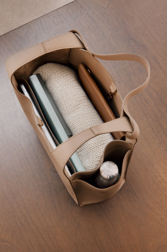 Top-down view of an open bag with a notebook, sweater, and a water bottle inside.