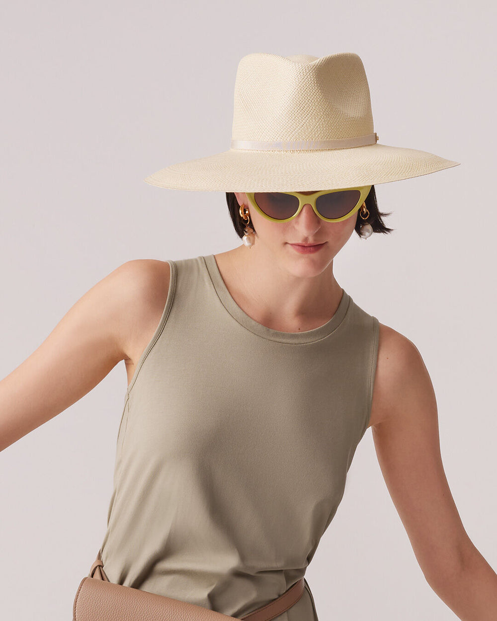 Woman wearing a wide-brimmed hat and sunglasses, carrying a shoulder bag.