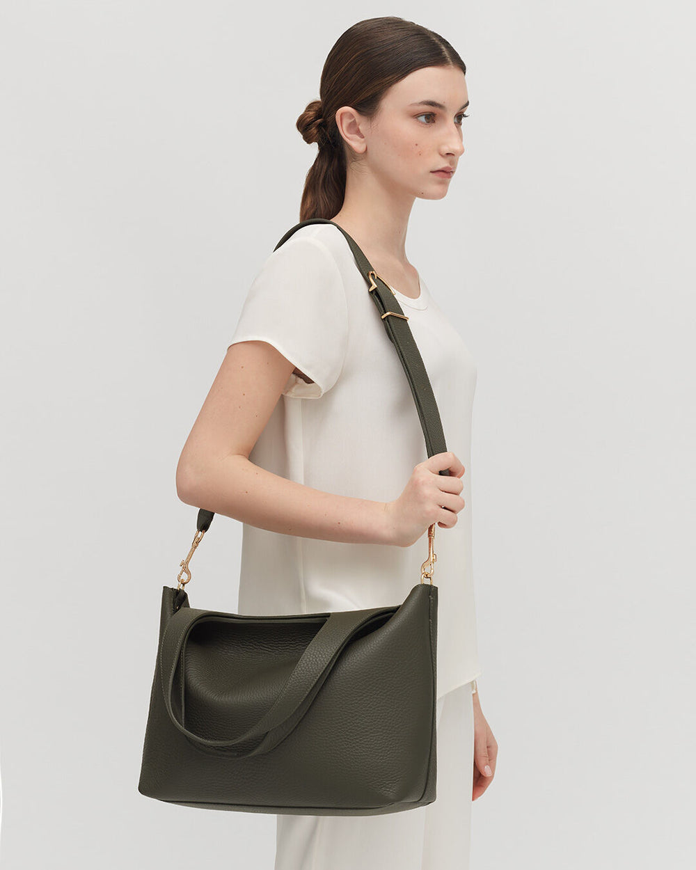 Woman standing with a shoulder bag, looking to the side.