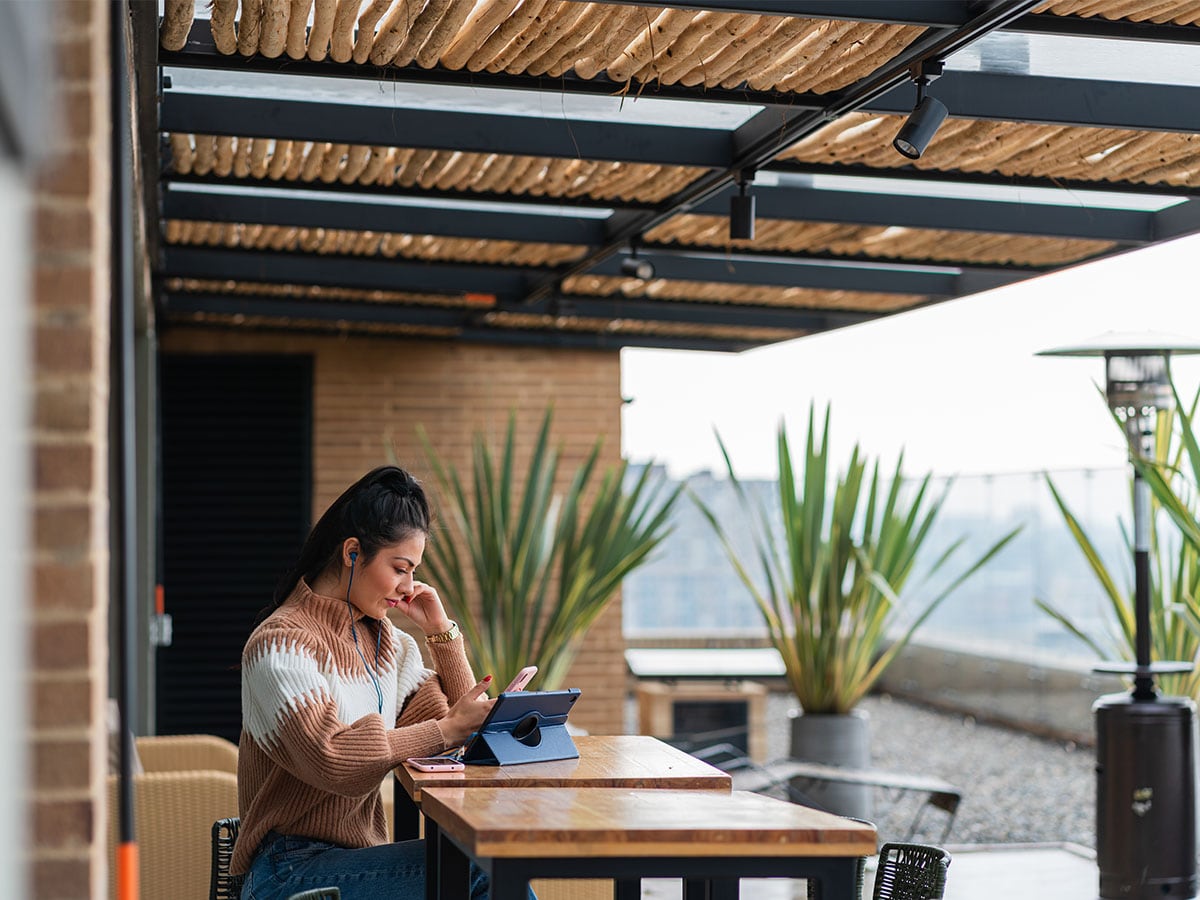 woman sitting at patio table with smart phone and tablet