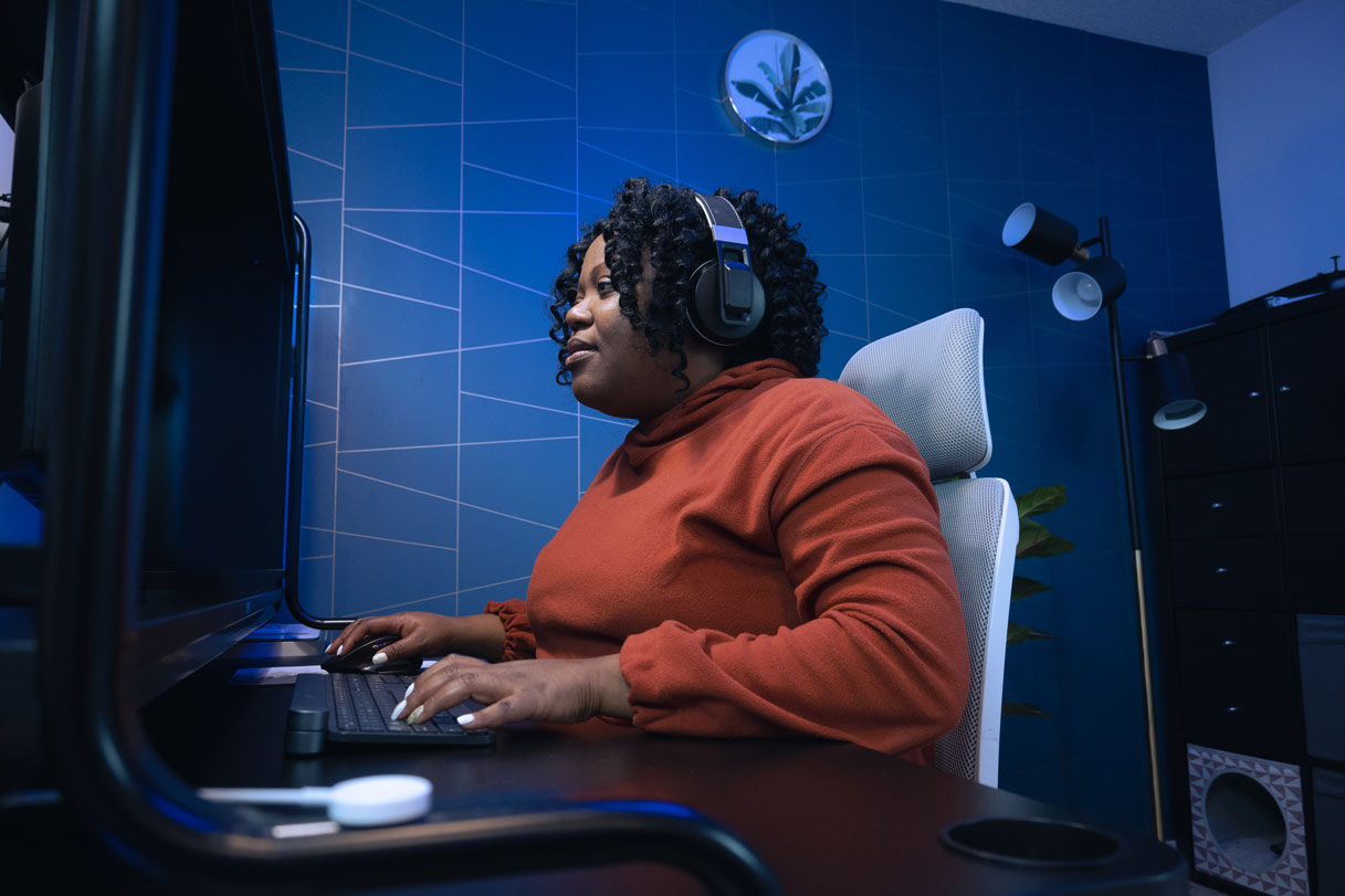 Une femme noire portant des écouteurs suit un cours des ateliers de création AWS sur son ordinateur de bureau
