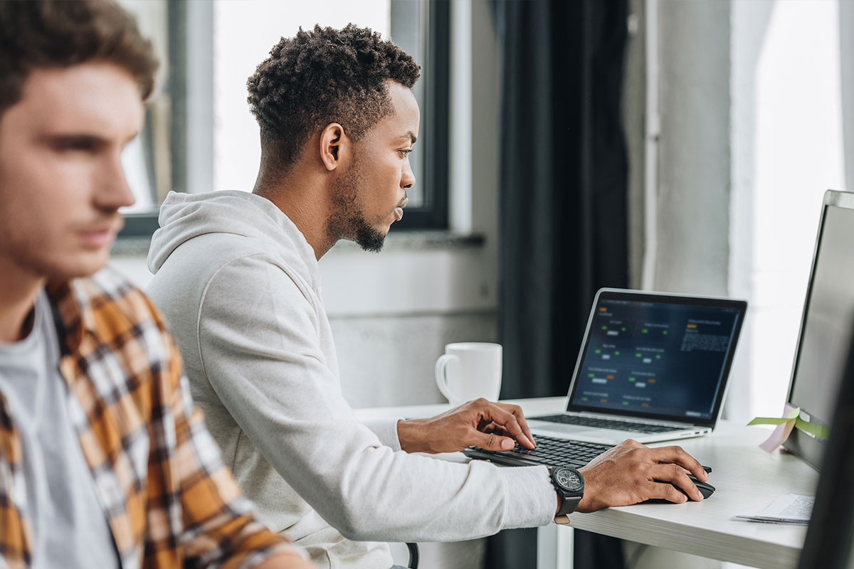 Two men sitting at table playing AWS Jam on laptops