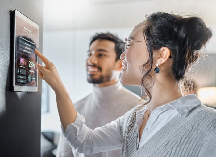 Image of a woman interacting with a screen on a wall in a home with a man standing next to her and smiling