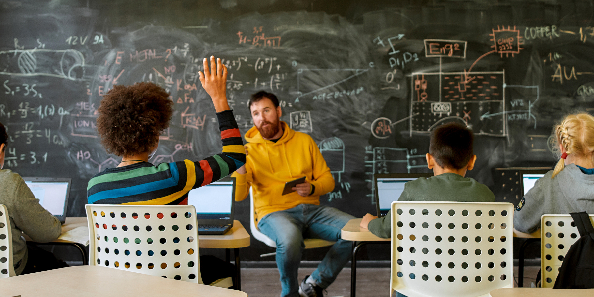 teacher in front of chalkboard lecturing students on laptop