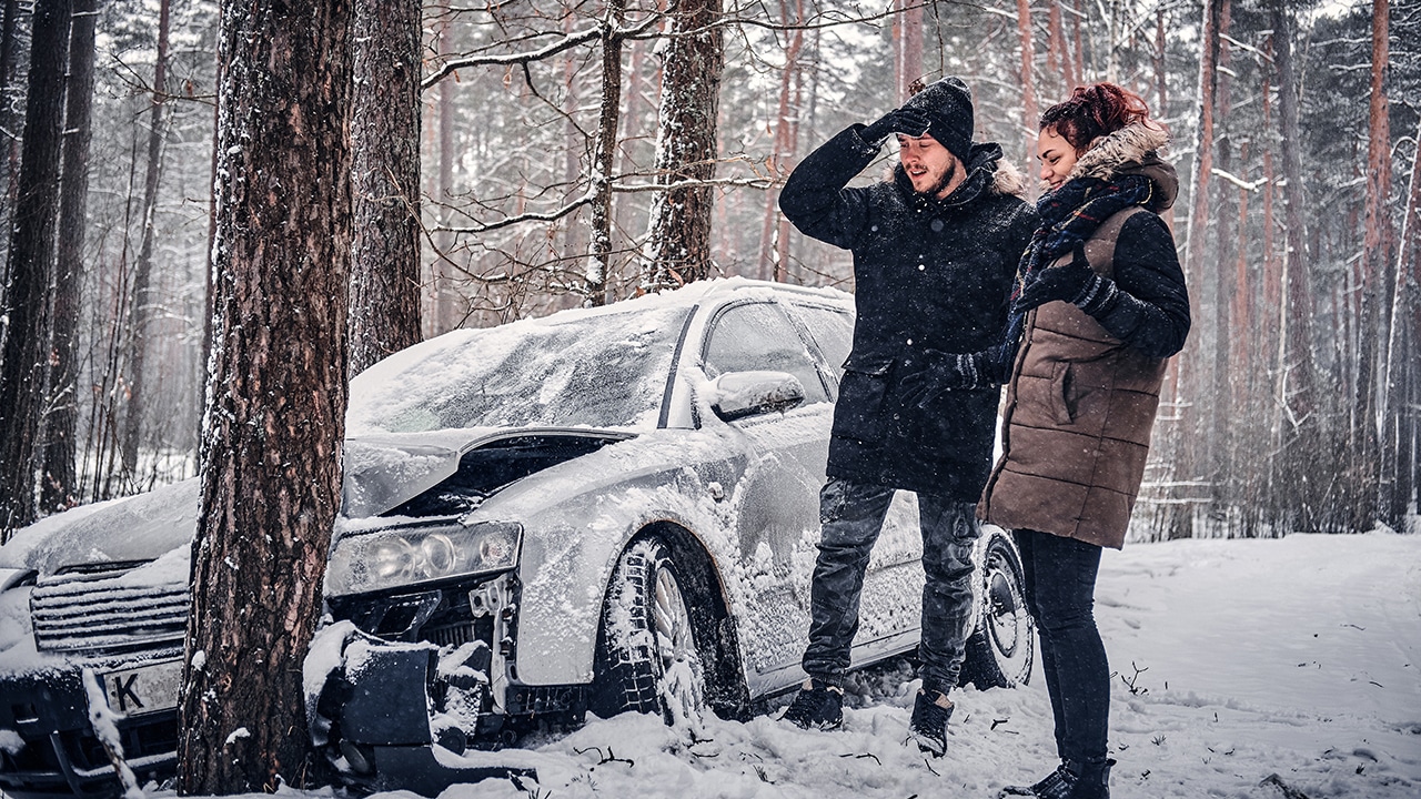 The car got into a skid and crashed into a tree on a snowy road. Shocked driver and passenger looking at car damage