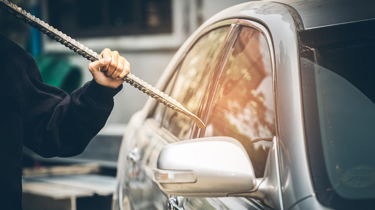 A robber dressed in black holding crowbar at a driver in a car.