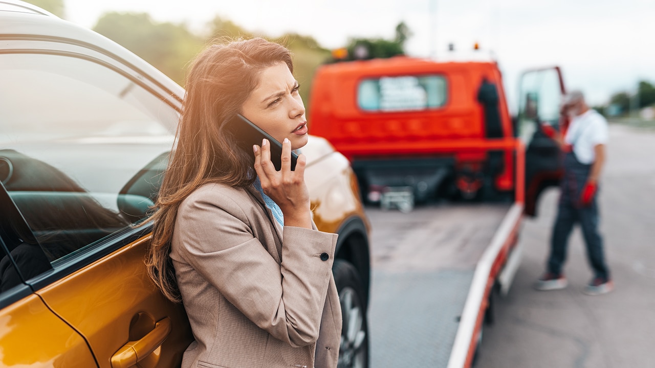 Elegant middle age business woman calling someone while towing service helping her on the road.