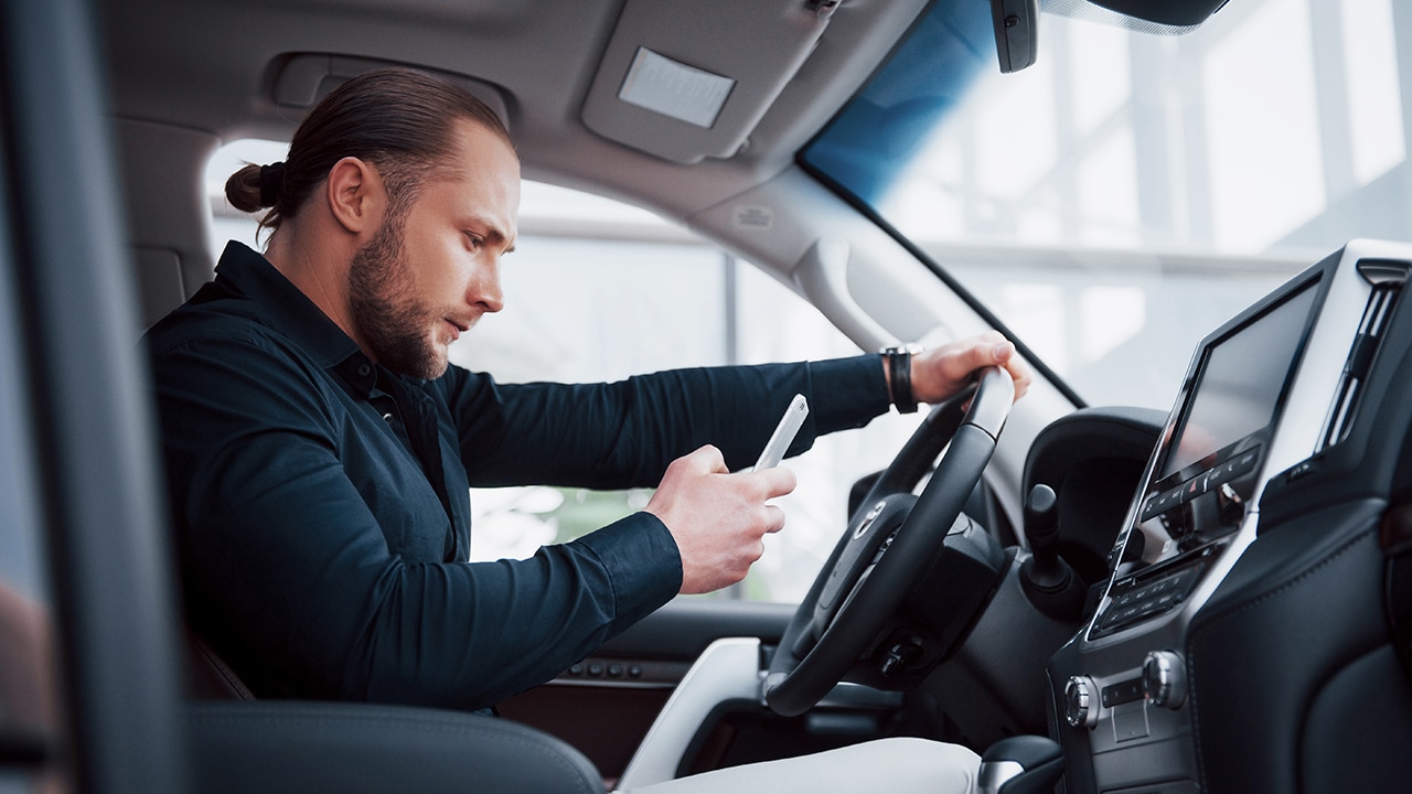 Satisfied young business man looking at mobile phone while driving a car.