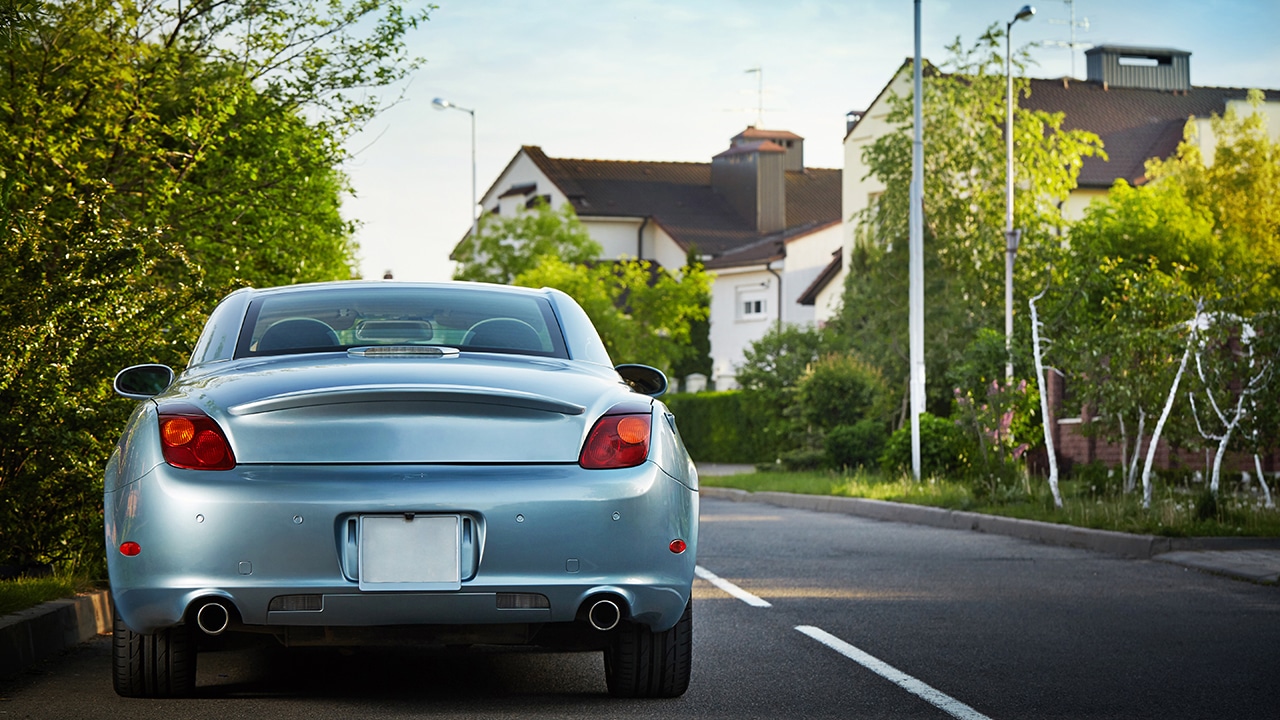 Blue car parked on the roadside near house, with natural backgrounds and with bright sunlight