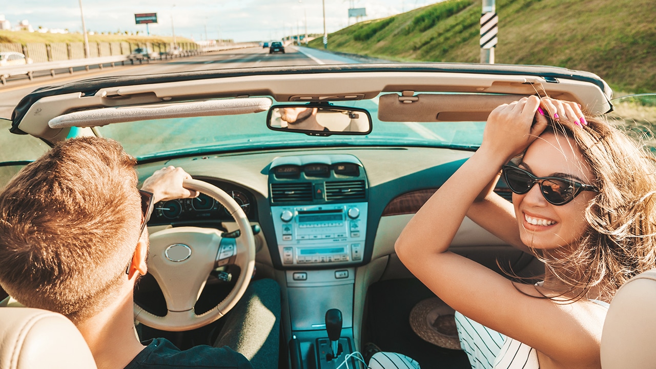 Portrait of two young beautiful and smiling hipster girls in convertible car. Sexy carefree women driving cabriolet. Positive models riding and having fun in sunglasses. Shows peace sign