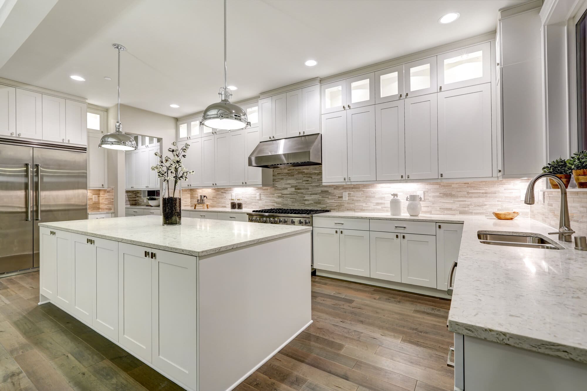 A white kitchen with white cabinets, white countertops, and hardwood floors.