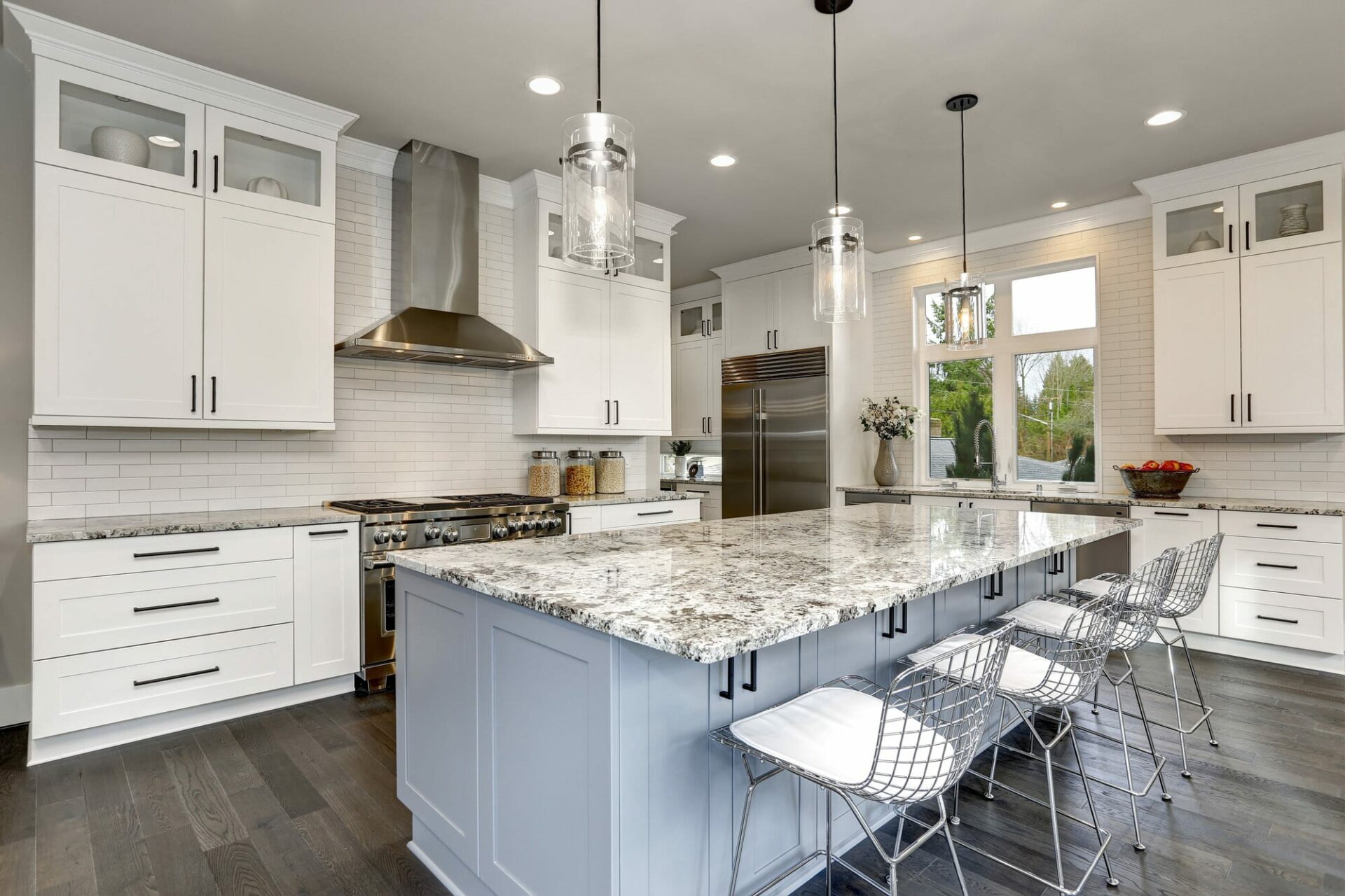 A kitchen with a grey granite countertop, white cabinets, and glass lighting fixtures.