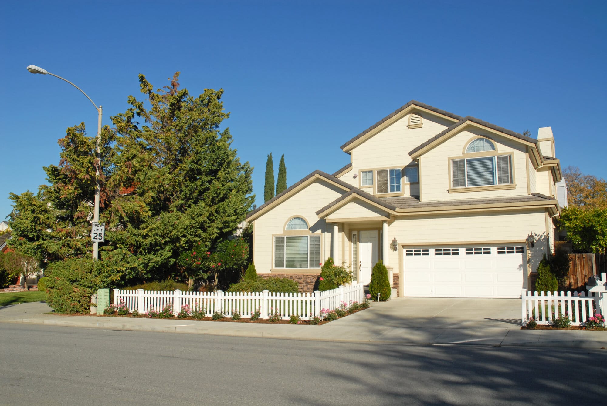 A California home painted cream with white picket fence and large green trees.